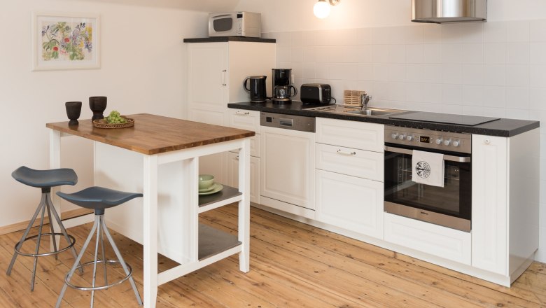 Moderne Küche mit weißer Einrichtung, Holzboden und kleinem Esstisch mit zwei Hockern.