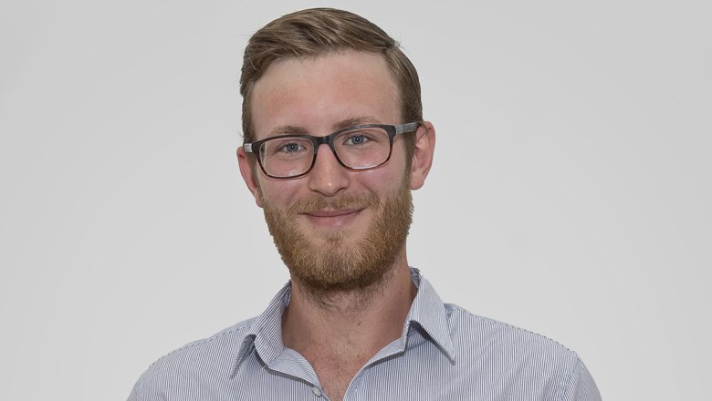 Portr&auml;t eines Mannes mit Brille und Bart in einem gestreiften Hemd vor neutralem Hintergrund.