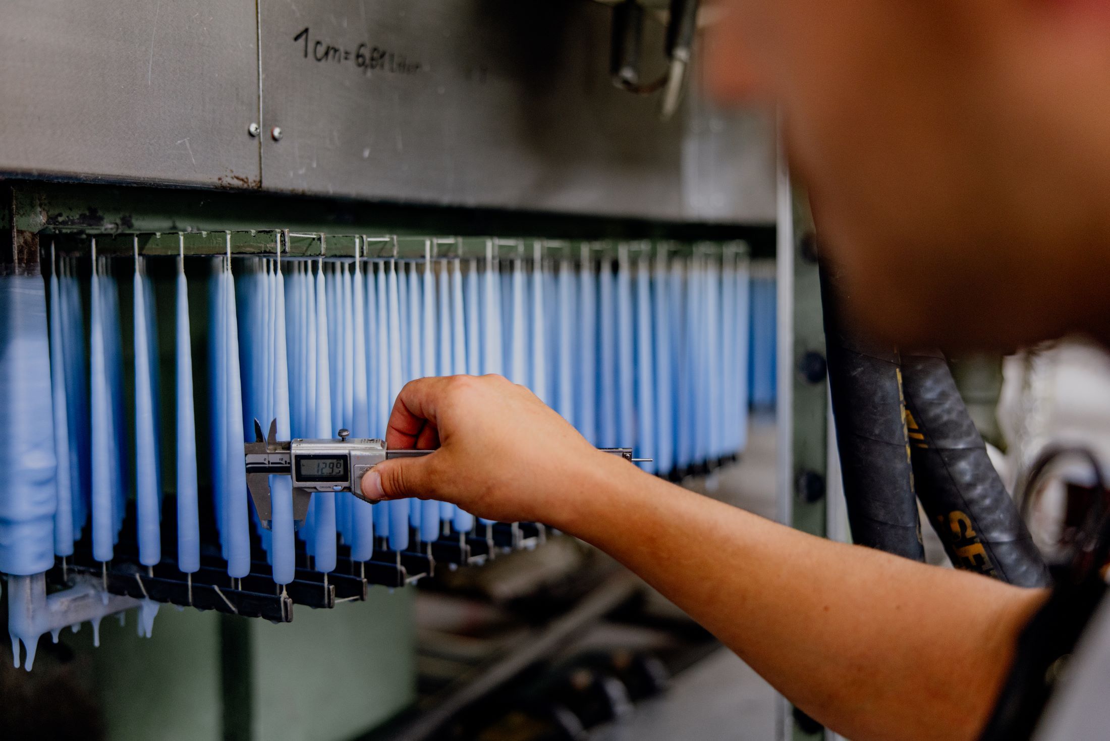 Eine Person misst die Dicke von blauen Kerzen mit einem Messschieber in einer Fabrik.