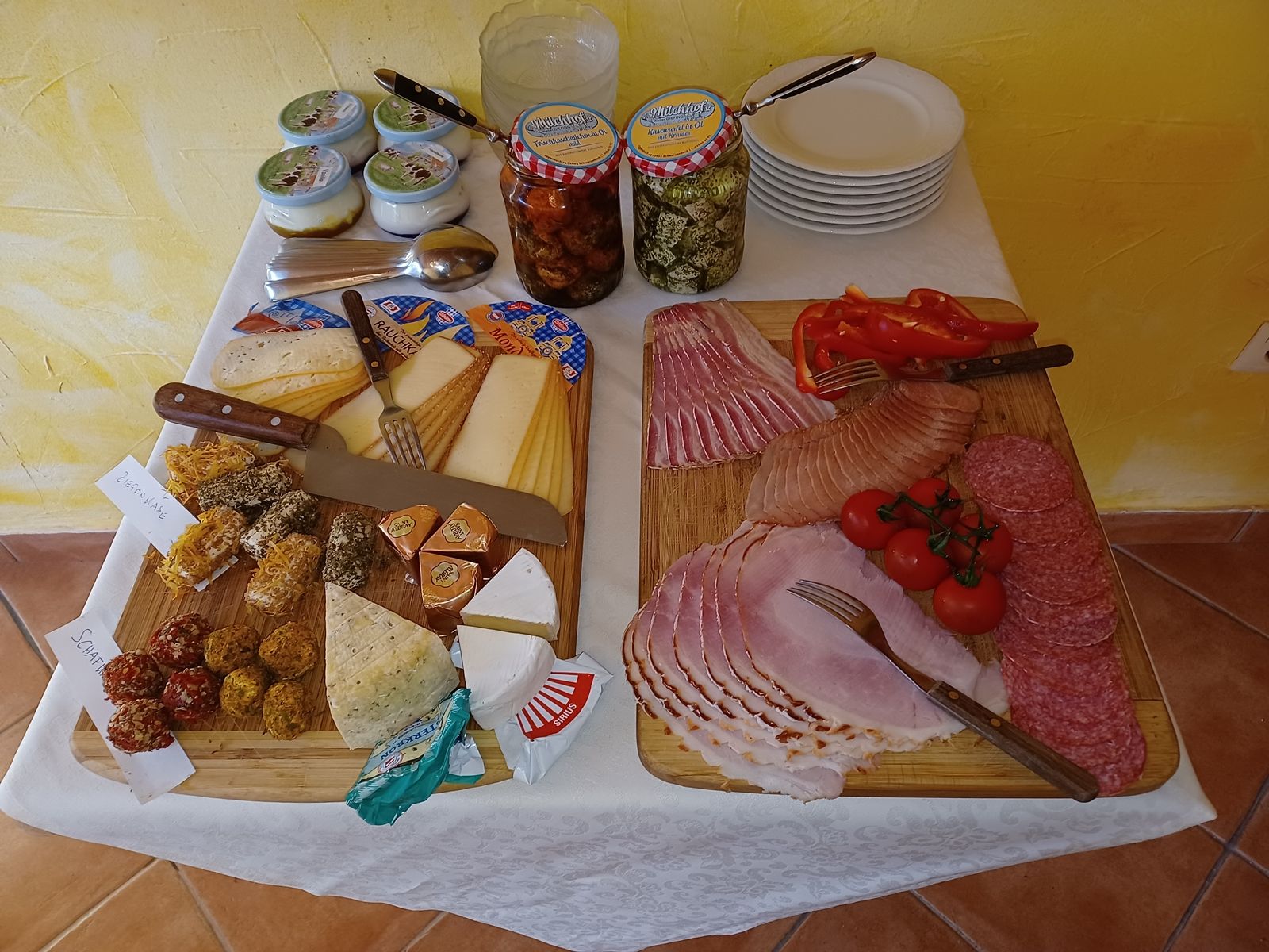 Frühstücksbuffet mit Käse, Aufschnitt, Tomaten und Paprika auf Holzbrettern.