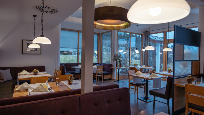 Innenansicht eines modernen Hotelrestaurants mit Holzm&ouml;beln und gro&szlig;en Fenstern.