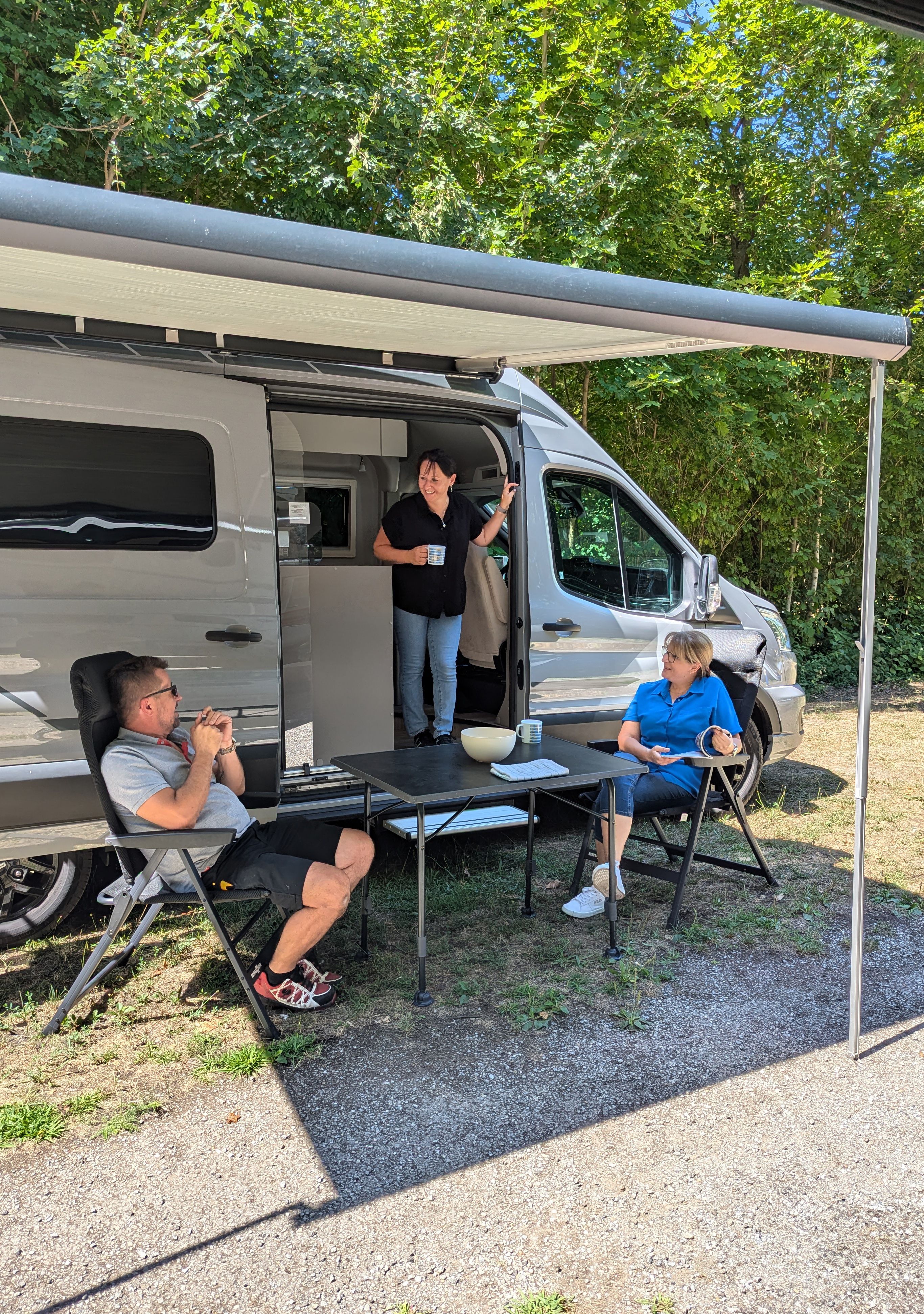 Drei Personen entspannen vor einem Wohnmobil im Freien.