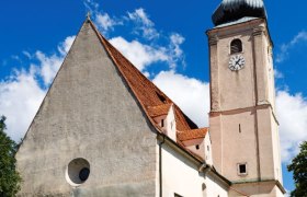 Pfarrkirche Wiesmath mit Turm, Friedhofsmauer aus Stein und Uhr vor blauem Himmel.