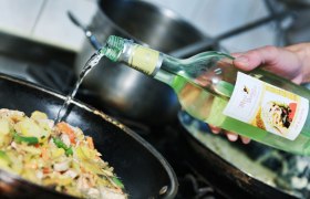 Eine Hand gie&szlig;t Most aus einer Flasche in eine Pfanne mit Gem&uuml;se.