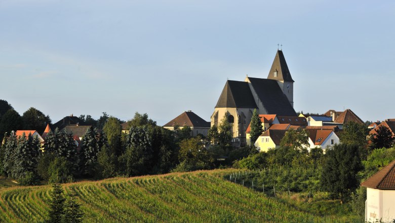 Landschaft mit Kirche und Dorf im Hintergrund, umgeben von Feldern und Bäumen.