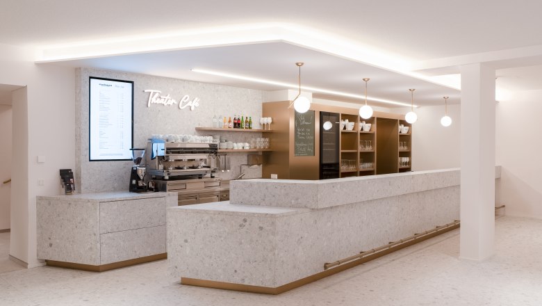 Modernes Theatercaf&eacute; im Stadttheater Wiener Neustadt mit heller Steinoptik, stilvollen Lampen und einladender Bar