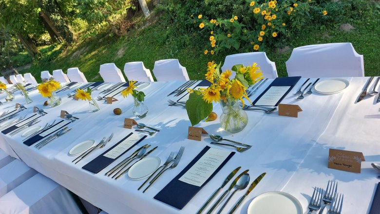 Festlich gedeckter Tisch im Freien mit wei&szlig;en Tischdecken, Sonnenblumen und Besteck.