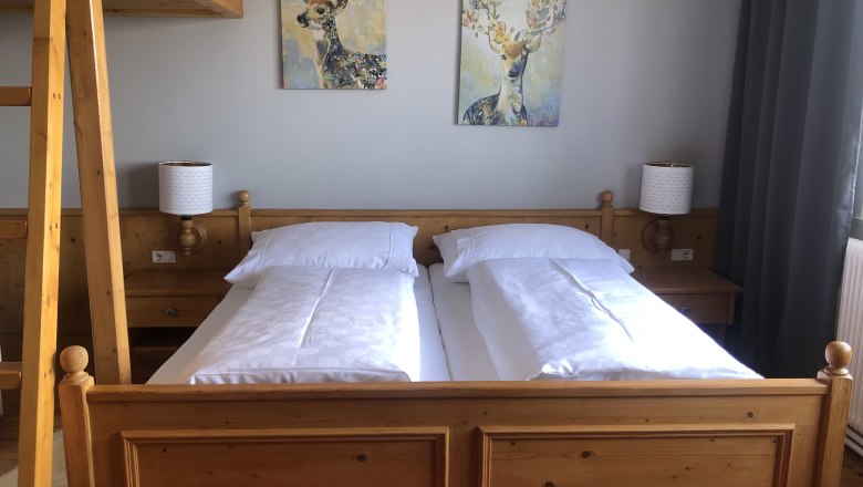 Gemütliches Schlafzimmer mit Holzmöbeln, Doppelbett, zwei Hirschbildern an der Wand und einer Leiter zu einem Hochbett.