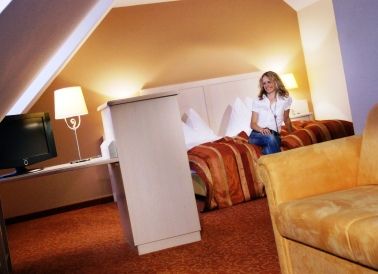 Frau sitzt auf einem Bett in einem gemütlichen Hotelzimmer mit warmen Farben.