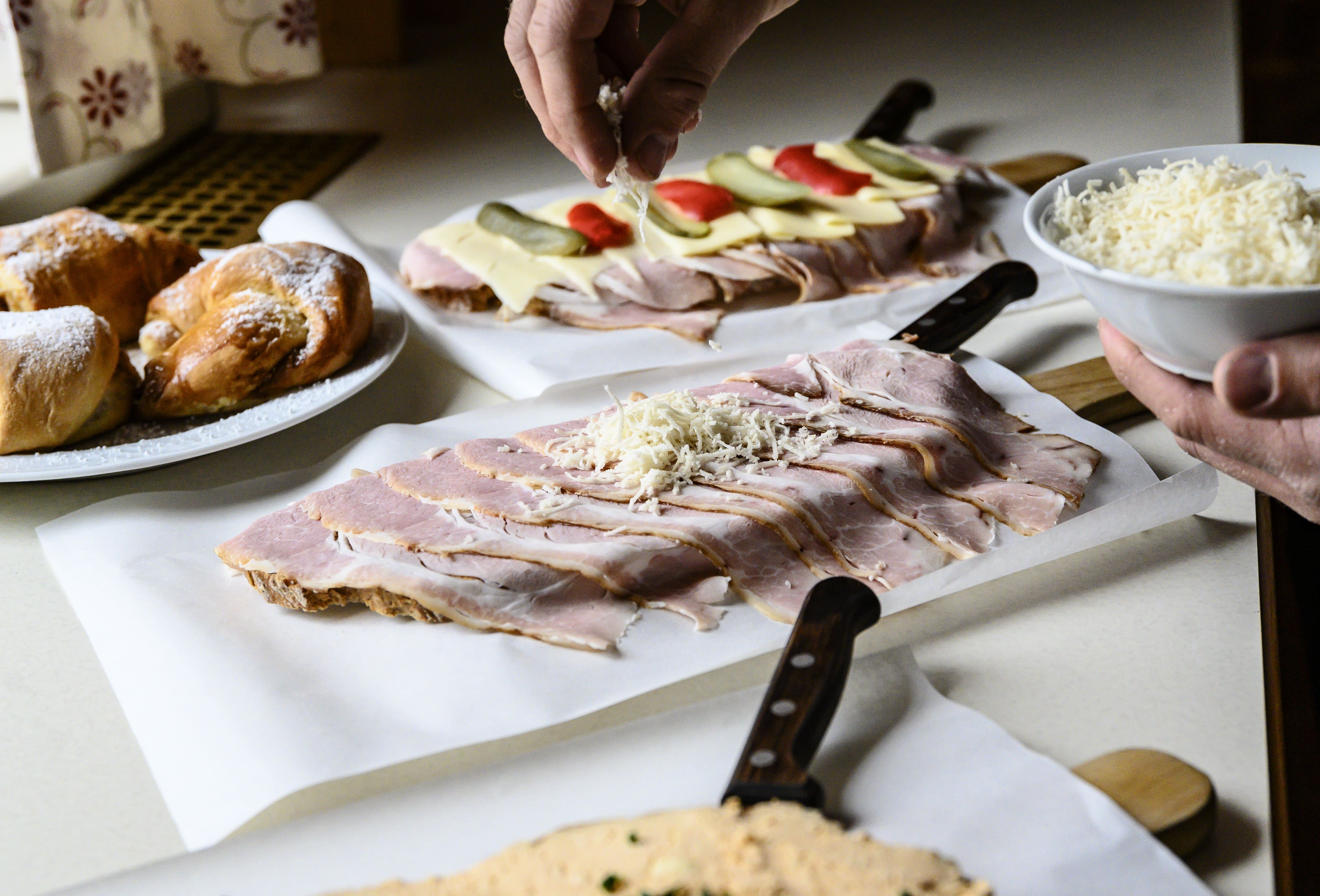 Zubereitung von belegten Broten mit Schinken und Käse, daneben Gebäck.