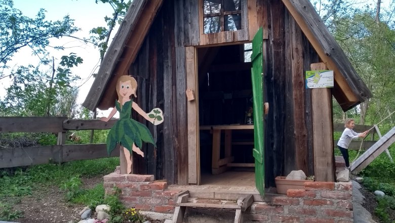 Kleines Holzh&auml;uschen mit gr&uuml;nem T&uuml;rrahmen und bemalter Figur daneben.