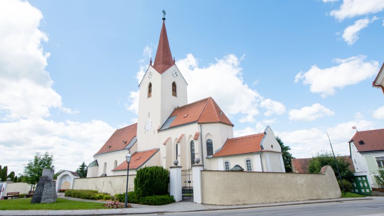 Kirche in Schweiggers mit rotem Dach und Turm vor blauem Himmel.