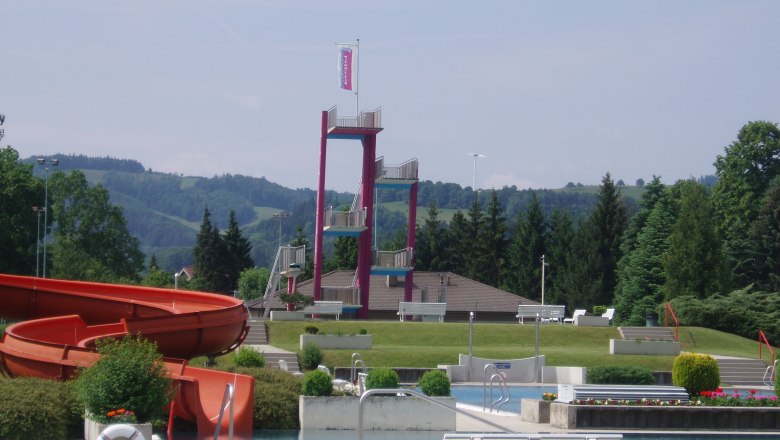 Ein Freibad mit Rutsche, Sprungturm und grüner Umgebung.