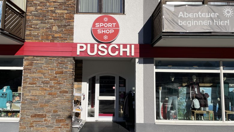 Eingangsbereich eines Sportgesch&auml;fts mit der Aufschrift 'PUSCHI' und einem Schild 'SPORT SHOP'. Schaufenster mit Sportbekleidung und Ausr&uuml;stung.