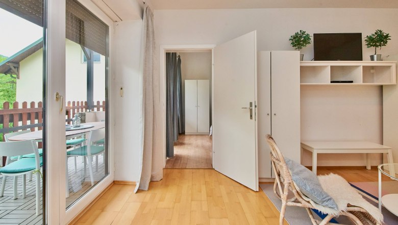 Helles Wohnzimmer mit Holzboden, Glastür zur Terrasse, weißen Möbeln und Pflanzen.