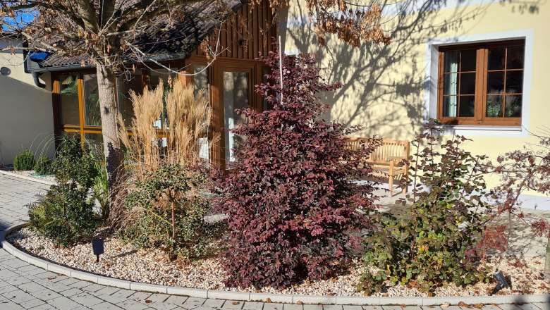 Ferienhaus zur alten Gärtnerei, © Tauchner Gartenansicht eines Ferienhauses mit Pflanzen und Bäumen vor gelber Fassade.