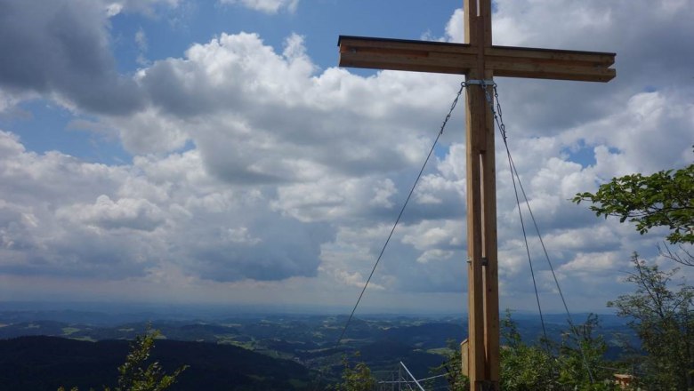 Gipfelkreuz auf dem Aussichtsberg Burgsteinmauer mit Blick auf bew&ouml;lkten Himmel und Landschaft.