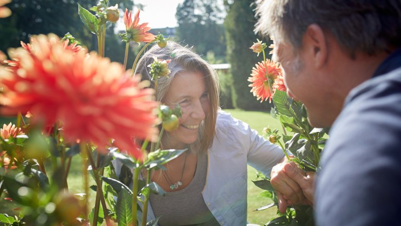 Zwei Personen lächeln sich zwischen blühenden Dahlien im Freien an.