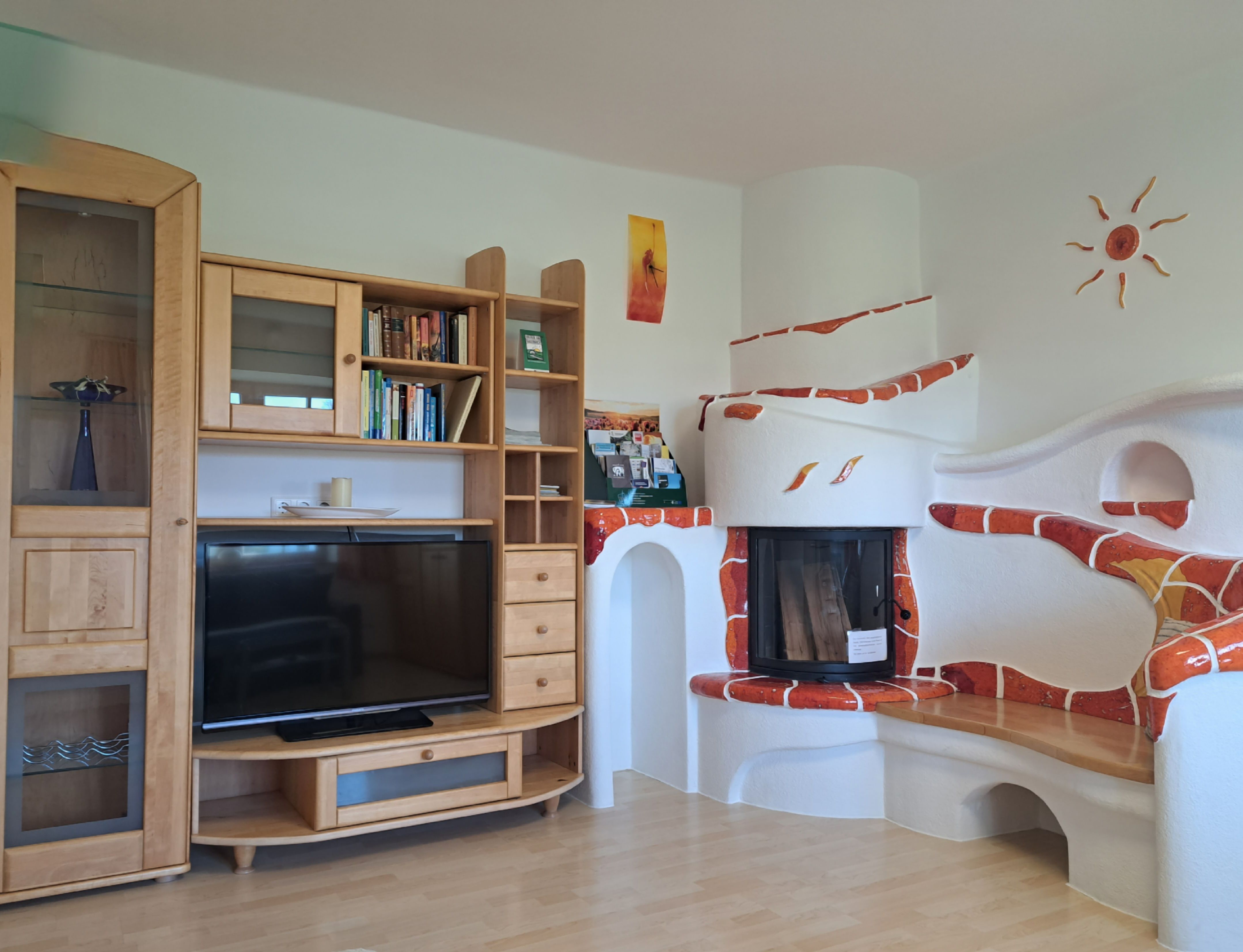 Wohnzimmer mit Kachelofen, hellem Wandverbau und Fernseher.