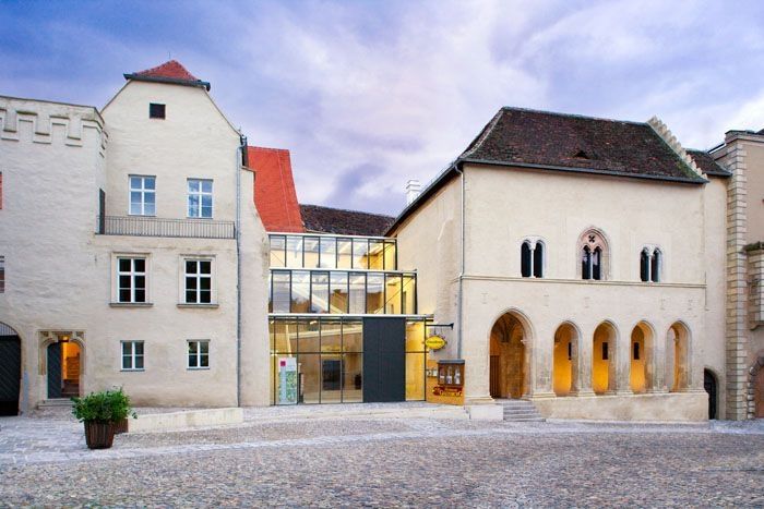 Historisches Gebäude mit modernem Glaszwischenbau, Kopfsteinpflaster im Vordergrund.