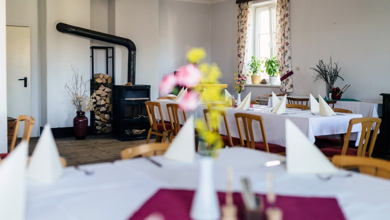Gem&uuml;tlicher Gastraum mit Holzofen, gedeckten Tischen und Blumen.