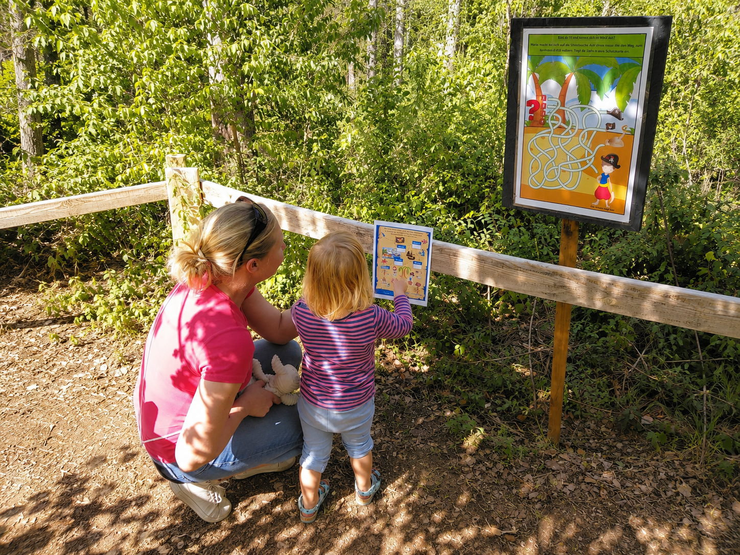 Eine Frau und ein Kind betrachten ein Rätsel auf einem Schild im Wald.