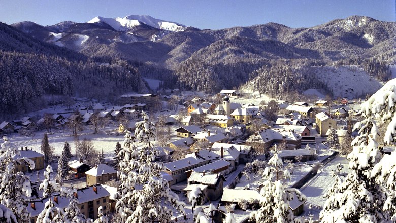 Winterliche Landschaft von St. Aegyd mit schneebedeckten H&auml;usern und Bergen im Hintergrund.