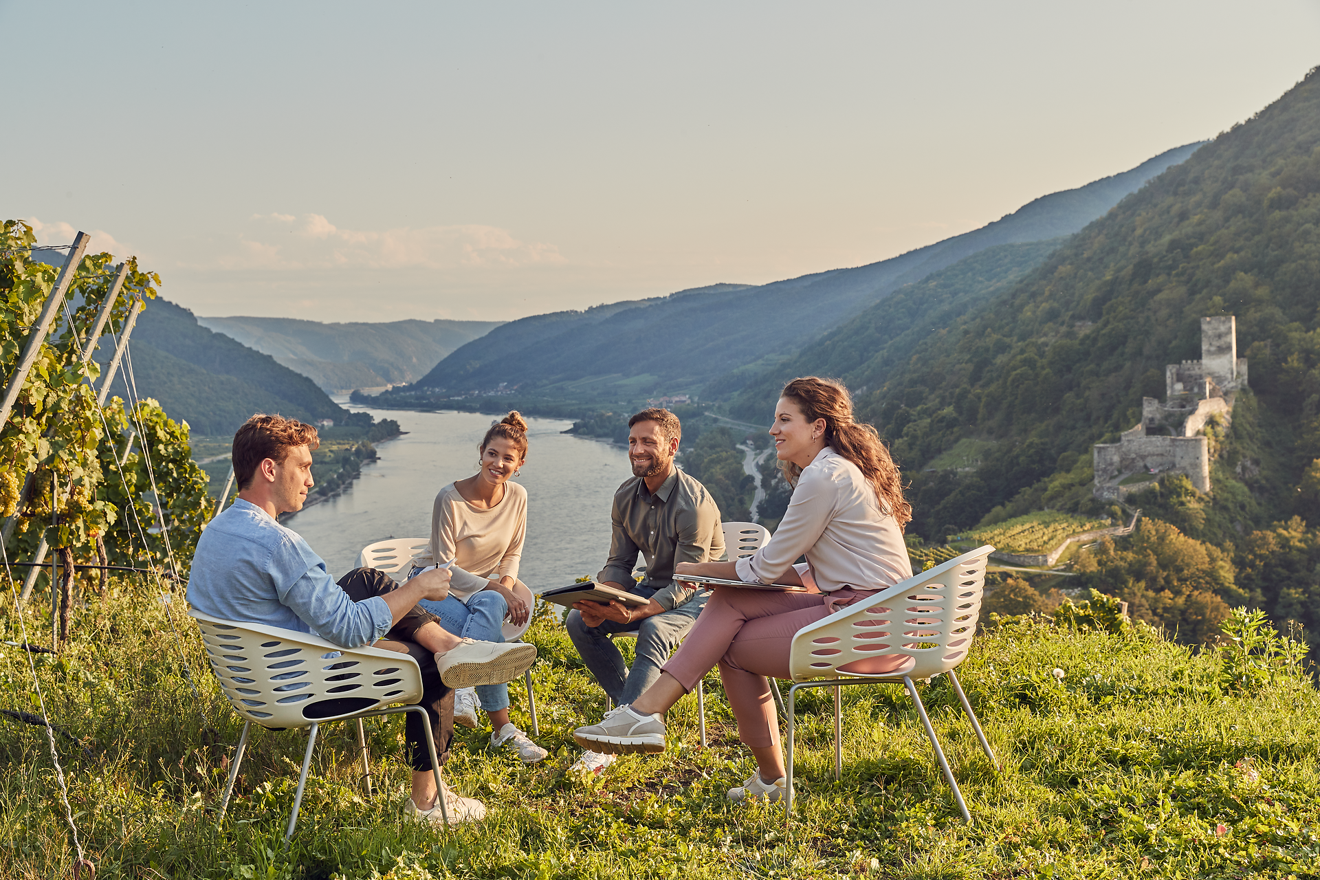 Inmitten der sanften Hügel und üppigen Weinreben versammeln sich Freunde, um die Schönheit der Natur und die Freude am Zusammensein zu genießen. Die goldene Abendsonne taucht die Landschaft in warmes Licht und schafft eine einladende Atmosphäre für unvergessliche Momente.