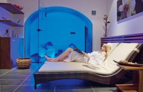 Frau entspannt auf einer Liege im Wellnessbereich mit blauer Beleuchtung.