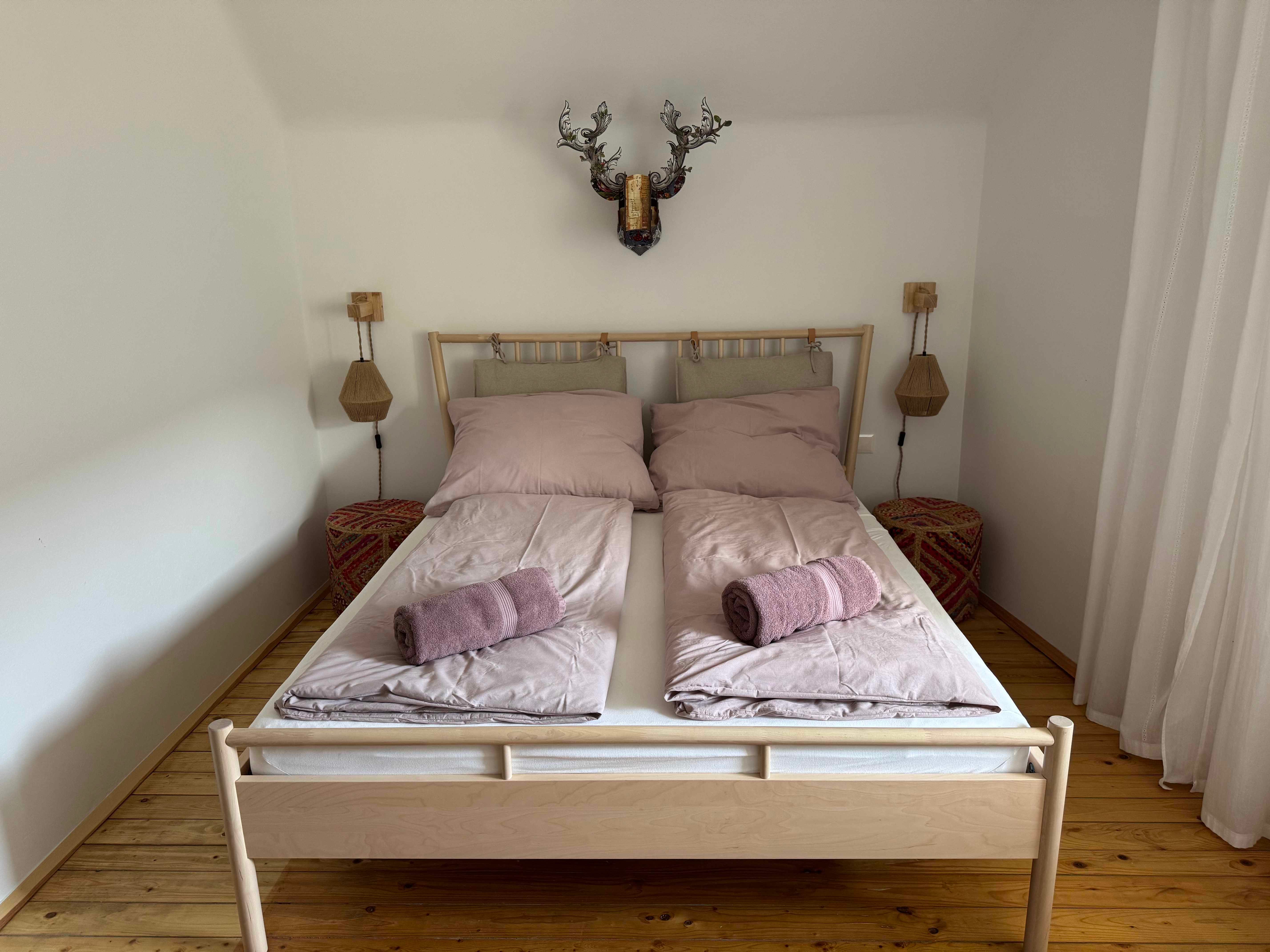 Schlafzimmer mit Doppelbett, rosa Bettwäsche und Handtüchern, Holzboden und Wanddekoration.