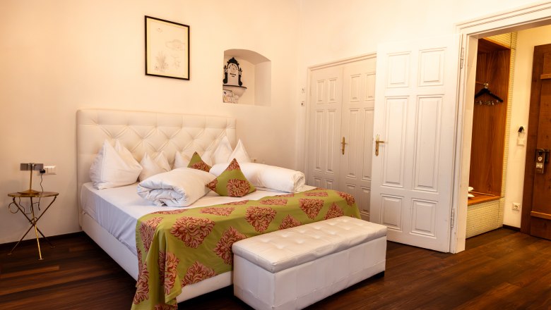 Elegantes Hotelzimmer mit großem Bett, weißen Möbeln und Holzboden.