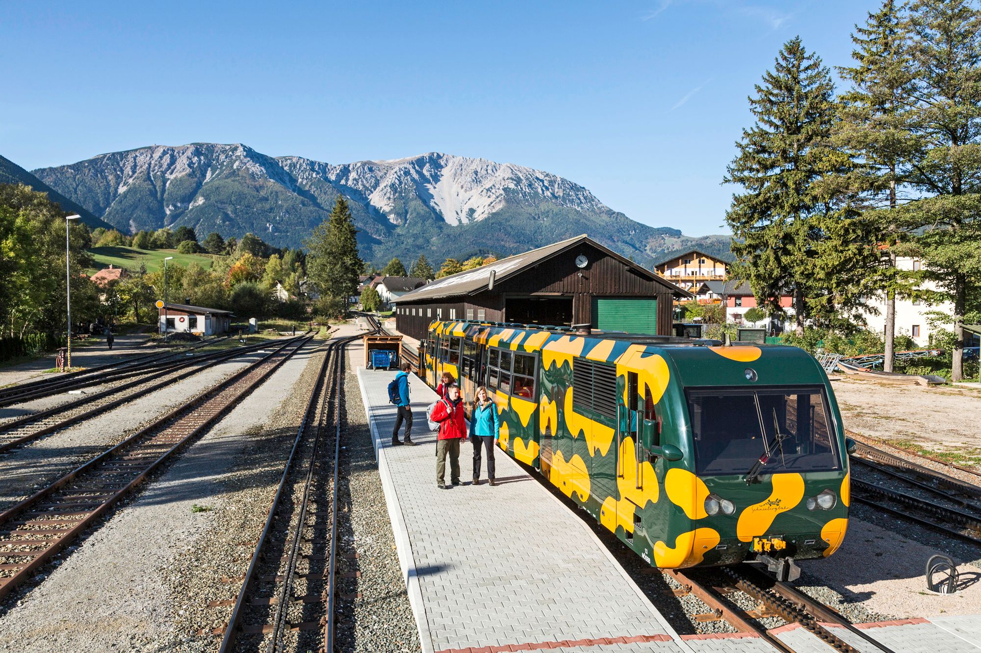 Bahnhof in Puchberg am Schneeberg mit einer bunten Zahnradbahn im Vordergrund und Bergen im Hintergrund.