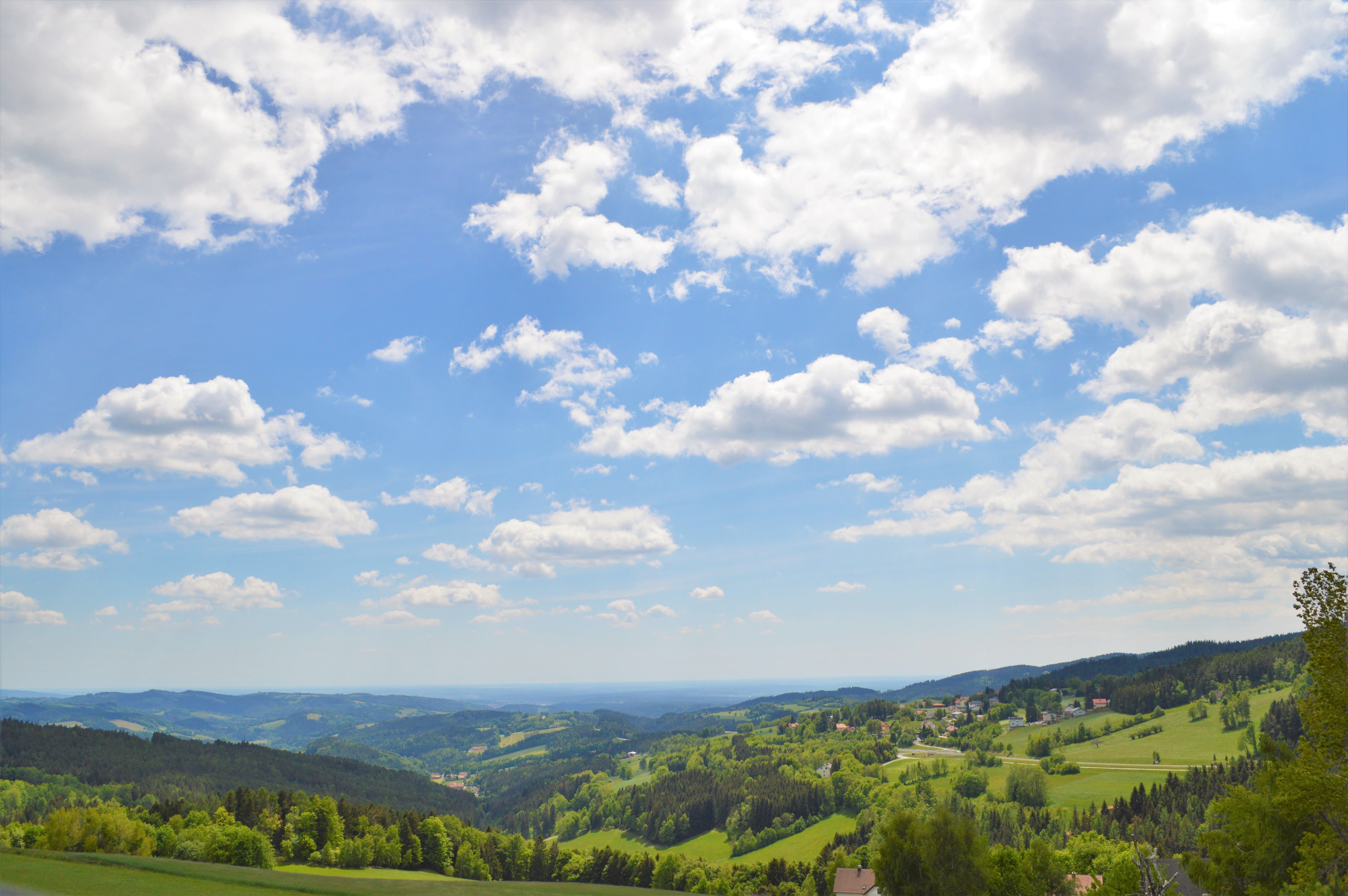 Panoramablick auf eine hügelige Landschaft mit Wäldern und Wiesen unter einem blauen Himmel mit weißen Wolken.