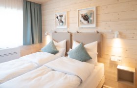 Gem&uuml;tliches Doppelzimmer mit zwei Einzelbetten, Holzw&auml;nden und moderner Dekoration.