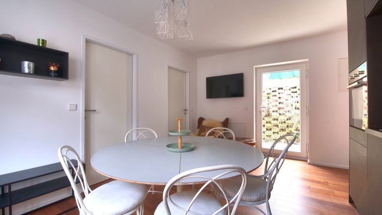 Moderner Essbereich mit rundem Tisch, wei&szlig;en St&uuml;hlen und h&ouml;lzernem Boden.