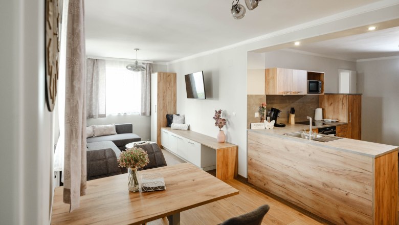 Moderne Wohnk&uuml;che mit Holzm&ouml;beln und grauem Sofa.