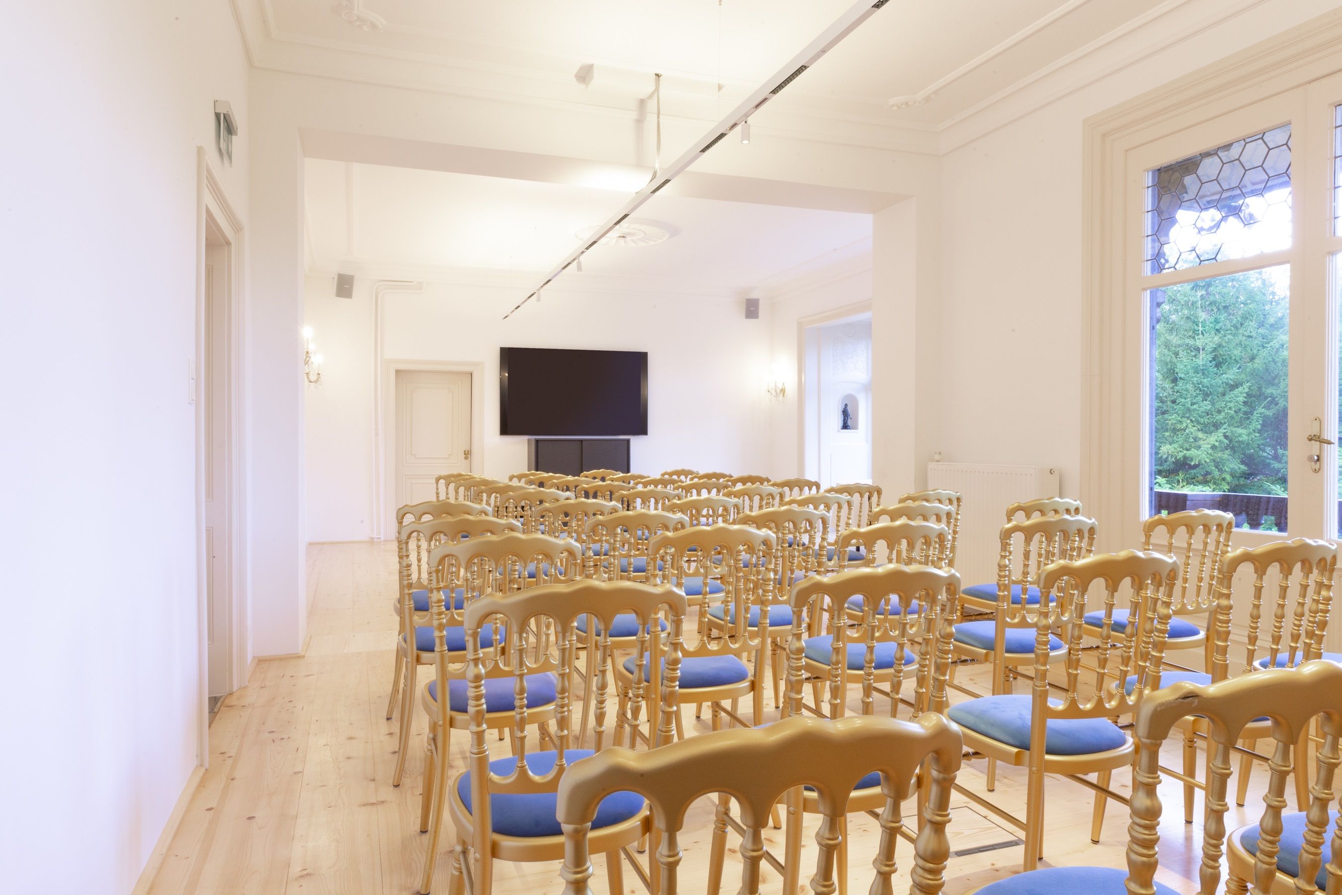 Ein heller Salon mit Stuhlreihen und einem großen Bildschirm an der Wand.