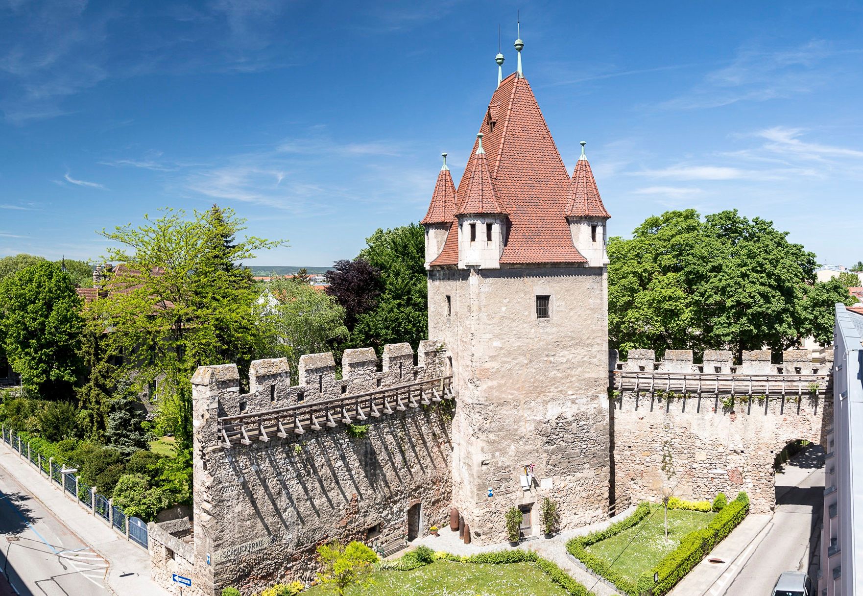 Reckturm mit rotem Dach und Steinmauer, umgeben von Bäumen und Straßen.