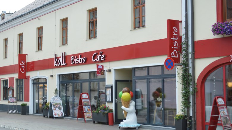 Au&szlig;enansicht des Koll Bistro Caf&eacute;s mit rotem Schild und Eisb&auml;rfigur mit Eis-Stanizel vor dem Eingang.
