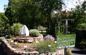 Kr&auml;uterspirale aus Steinen mit Pflanzen und einem Schild mit der Aufschrift 'Geheimtipp'.