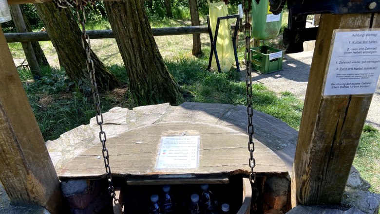 Ein Brunnen mit einer Holzkonstruktion, in dem Flaschen gelagert sind.