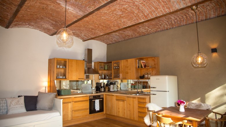 Gem&uuml;tliche K&uuml;che mit Holzm&ouml;beln, Ziegeldecke und Esstisch.
