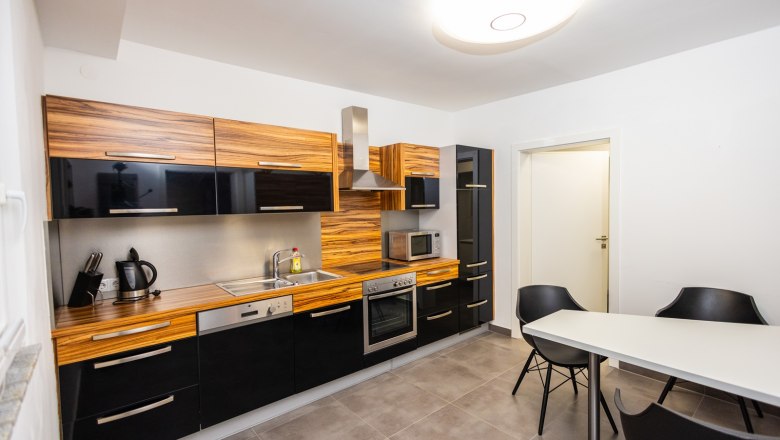 Moderne Küche mit Holz- und schwarzen Hochglanzfronten, Esstisch und Stühlen.