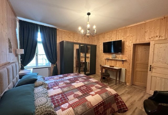 Gem&uuml;tliches Hotelzimmer mit Holzw&auml;nden, Doppelbett, Schreibtisch, Kleiderschrank und Flachbildfernseher.
