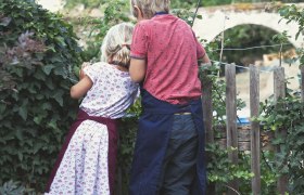Zwei Kinder stehen auf einer Bank und schauen über einen Zaun in einen Garten.