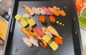Ein schwarzes Tablett mit einer Auswahl an Sushi, darunter Nigiri und Maki, dekoriert mit Kaviar und Kräutern.