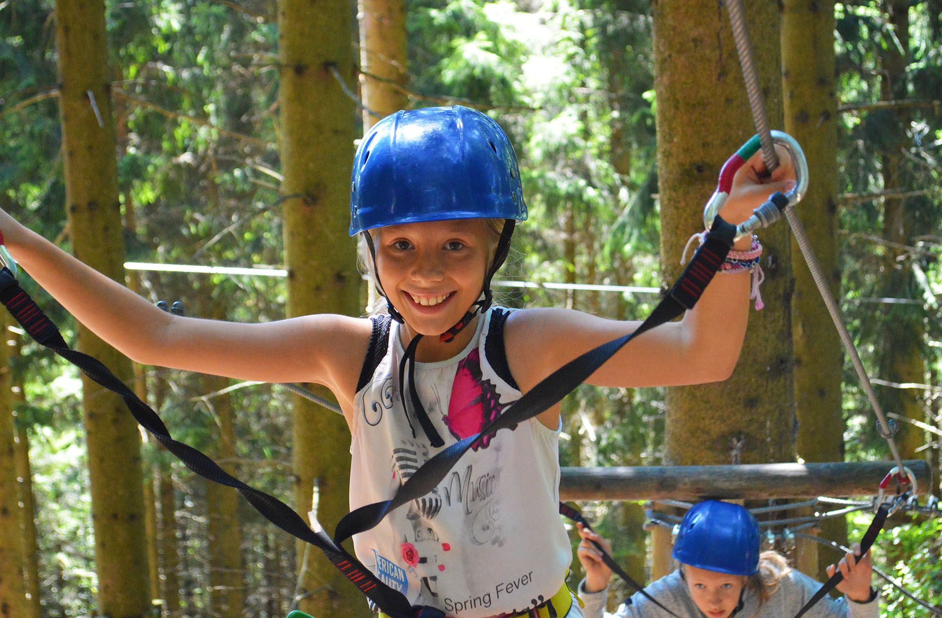Ein Mädchen mit blauem Helm balanciert auf einem Kletterparcours im Wald.