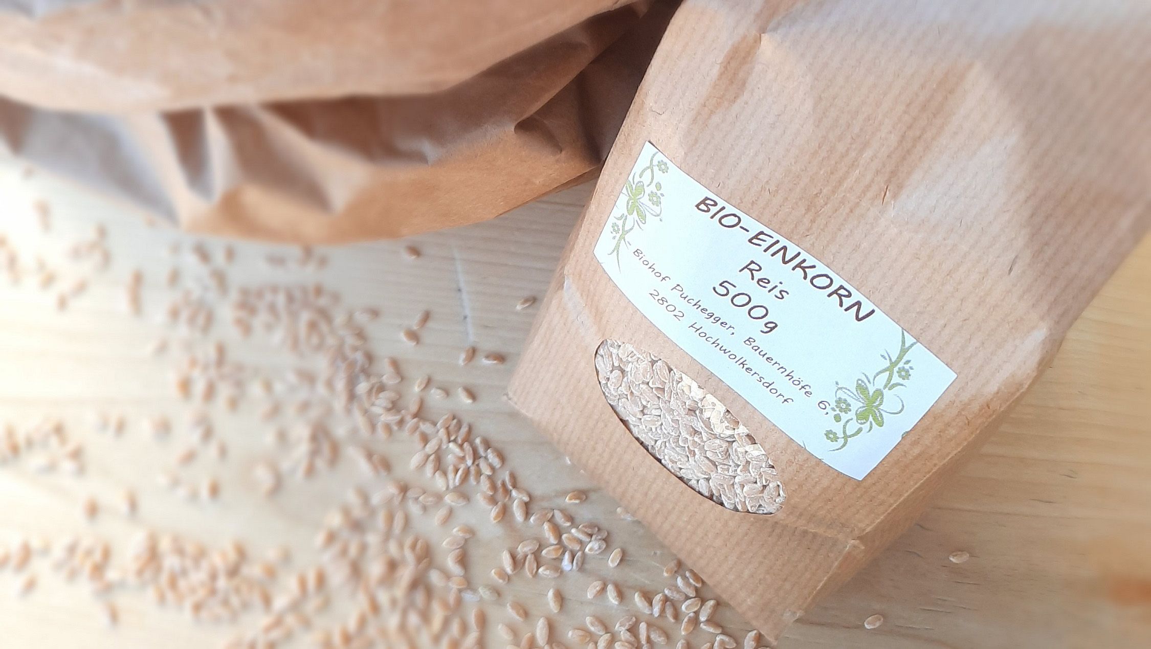 Eine Packung Bio-Einkorn Reis auf einem Holztisch umgeben von Reiskörnern.