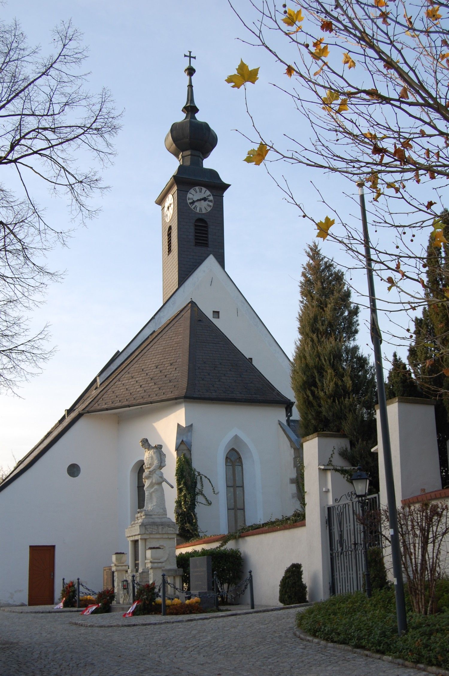 Gotische Kirche in Kirchstetten mit Turm und Statue im Vordergrund.