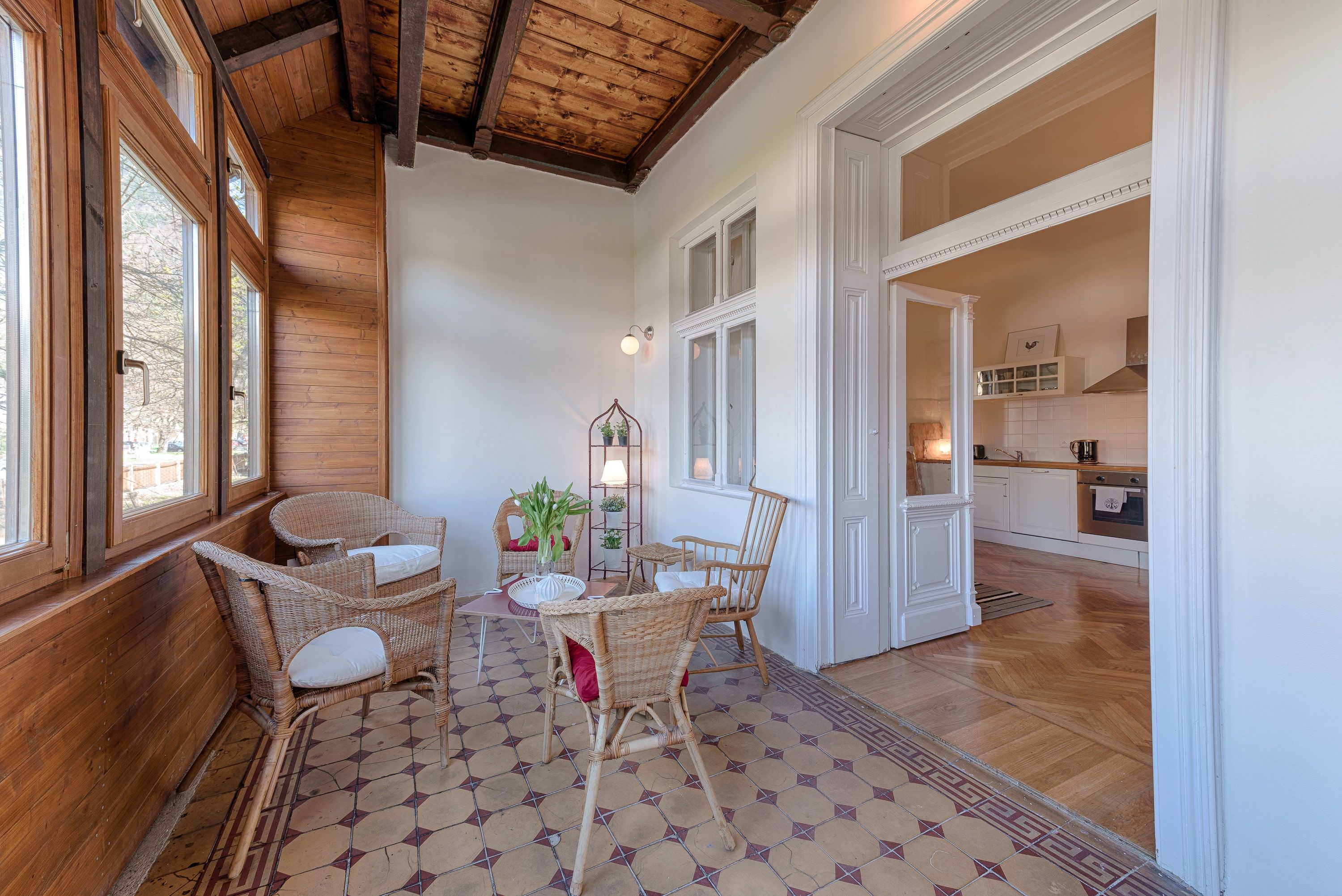 Wintergarten mit Holzwänden, Rattanmöbeln und Blick in eine Küche.